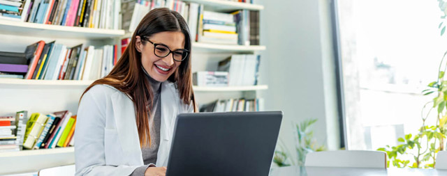 A woman in glasses smiles at a laptop.
